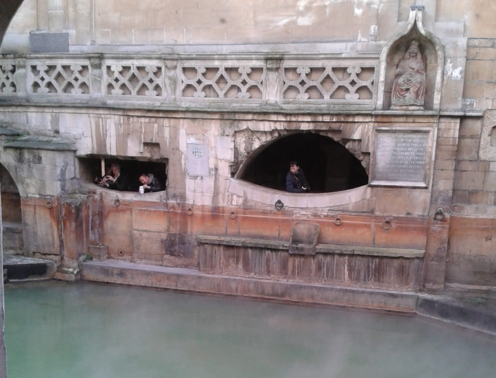 The Roman Baths at Bath are one of the best Roman sites to visit in the Cotswolds. Here, visitors are viewing the steaming King's Bath from the 2nd century AD spring building.