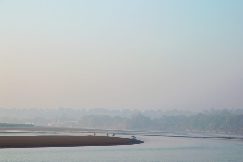 In the hazy morning light, surfers wait patiently for the tidal bore (wave) to reach them.